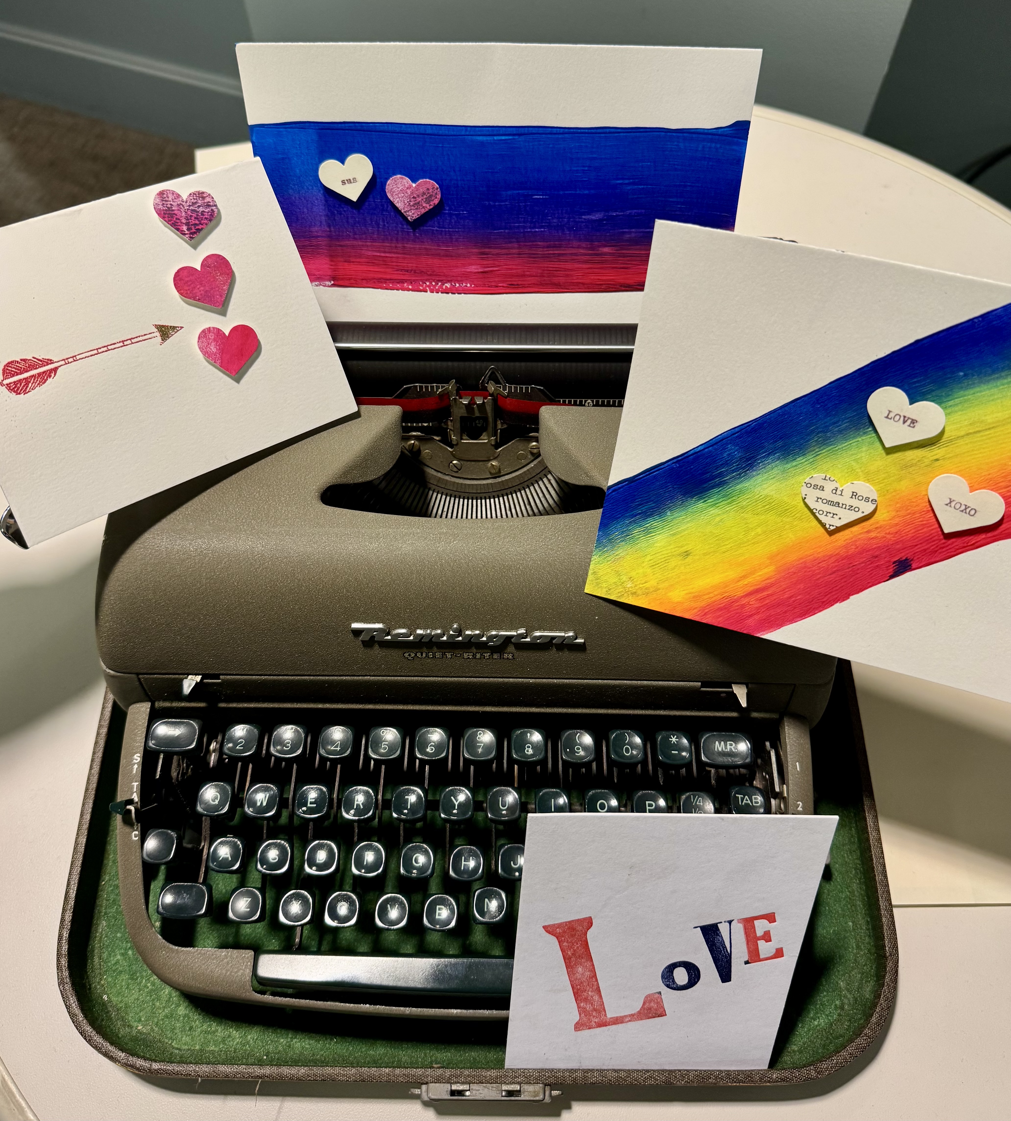 Color photograph of a 20th century manual typewriter with 4 colored cards depicting valentine themes. One card reads "LOVE"